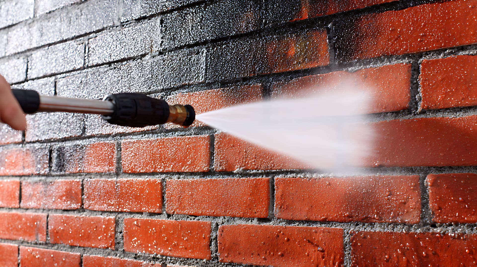 Pressure washer removing grime from a red brick commercial wall, dramatic before and after in one frame